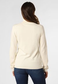 Cremfarbener Rollkragenspullover, gerippte Bündchen und Saum, weiche Textur, taillierte Passform, getragen mit dunkelblauen Jeans, Rückansicht.