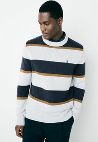 Knit sweater featuring navy, white, and gold stripes, crew neck, ribbed cuffs and hem, with a small logo on the chest.