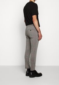 Harmaat ruudulliset housut ovat slim fit -malliset, joissa on punaisia yksityiskohtia kuosissa. Niissä on takatasku ja ne on yhdistetty mustiin kenkiin.