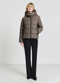 Brown puffer jacket with a high collar, featuring quilted sections and front zip. Paired with black pants and pointed black shoes.