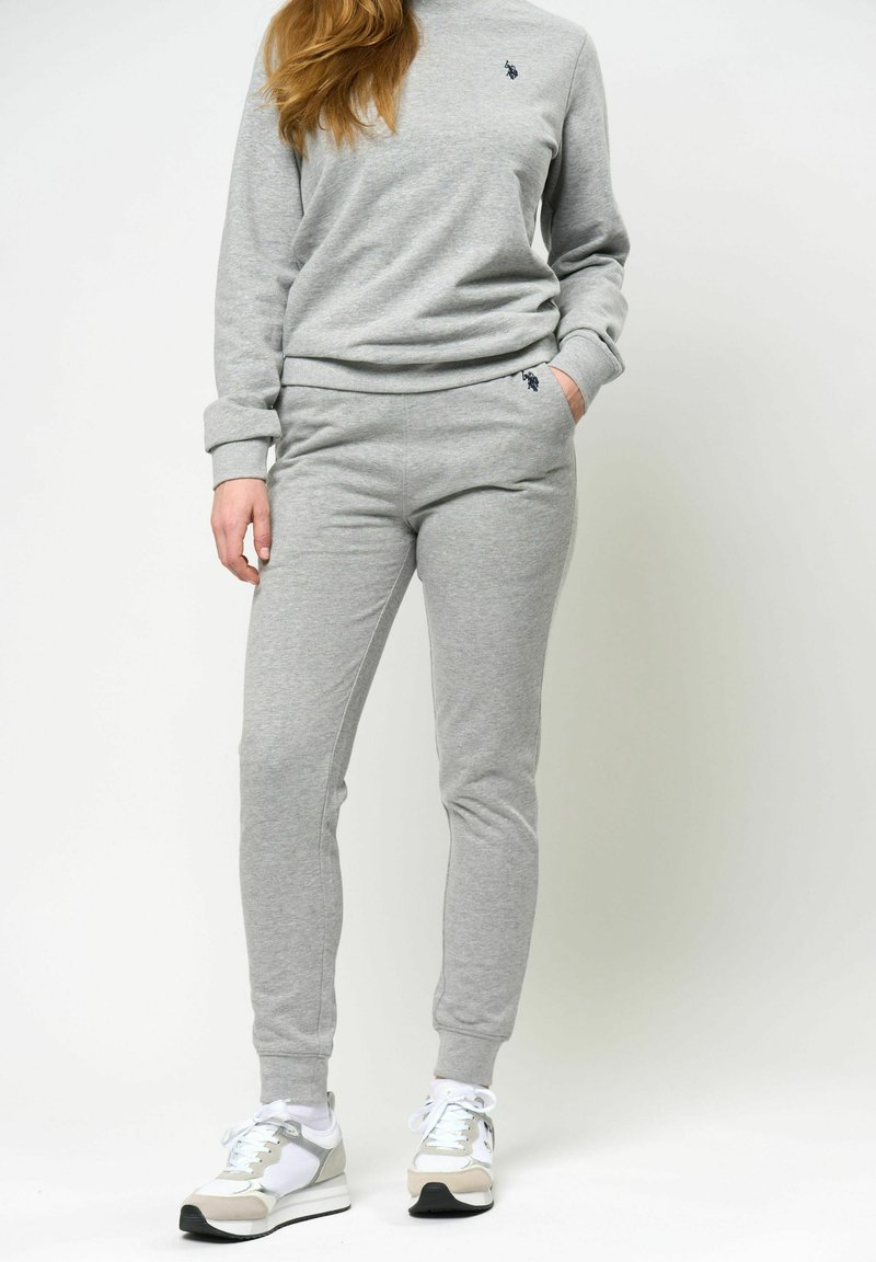 Grå sweatshirt och byxor i mjukt tyg, med en liten logotypdetalj. Matchas med sportiga sneakers i grått och vitt.