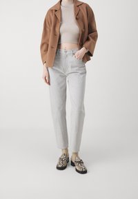 Blazer marrón de gran tamaño, top corto beige de canalé, vaqueros gris claro de pierna recta y zapatos estampados con suela negra. Fondo liso.