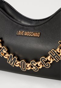 Svart veske i faux skinn med en gullkjede som har bokstaver som staver "LOVE MOSCHINO" og en gull logo-plakett på fronten.
