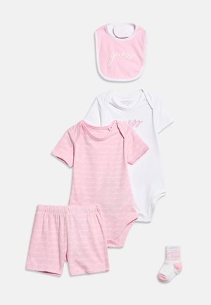 Conjunto de ropa para bebé en rosa y blanco que incluye dos bodies, pantalones cortos, un babero y un calcetín, todos con la marca "Guess" y tela suave.