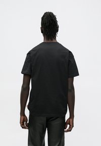 Čierne bavlnené tričko s krátkym rukávom a okrúhlym výstrihom, s jednoduchým dizajnom na zadnej strane a voľným strihom. Bez viditeľných log alebo vzorov.