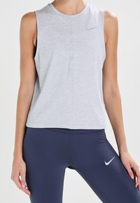 Camiseta deportiva sin mangas de color gris claro con cuello redondo y logo sutil de Nike; combinada con leggings azul marino que llevan un logo similar.