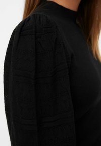 Pull noir avec des manches bouffantes en dentelle texturée, orné d'un motif géométrique, corps ajusté et col côtelé.