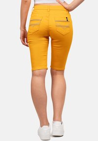 Gele denim bermuda shorts met achterzakken en decoratieve stiksels. De stof is rekbaar en aansluitend, eindigend net boven de knie.
