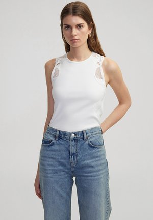 Witte geribde tanktop met kantdetail op de schouders en zijkanten, gecombineerd met hoog uitgesneden lichtblauwe denim jeans met een knoopsluiting.