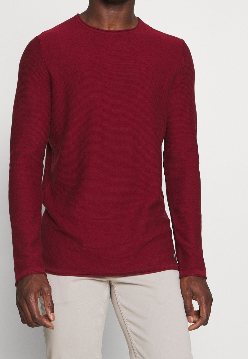 Camicia bordeaux a maniche lunghe in tessuto lavorato a maglia, con scollatura rotonda e design aderente. Presenta una finitura dell'orlo discreta e un leggero restringimento.