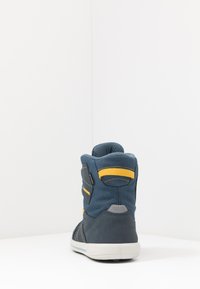 Sneaker alta in tessuto blu scuro con accenti gialli. Presenta una tomaia testurizzata, un collo imbottito e una suola in gomma.