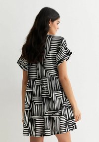 Zwart-witte jurk met een gelaagd ontwerp en gedurfde gestreepte patronen. Korte mouwen en een uitlopende silhouet zorgen voor een losse pasvorm.