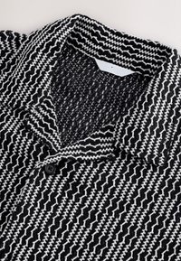 Giacca con motivo in bianco e nero realizzata in un tessuto intrecciato e testurizzato. Presenta un collo con rever e un bottone nero sul davanti.