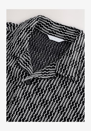 Fekete-fehér mintás dzseki texturált, szőtt anyagból. Galléros nyakkivágással és az elején fekete gombbal rendelkezik.