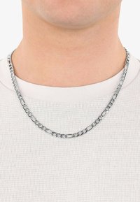 Collana in metallo argentato con maglie interconnesse, indossata sopra una maglietta bianca a girocollo con texture, che mette in risalto la lucentezza e il design della collana.