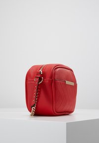 Czerwony pikowany torebka crossbody z sztucznej skóry z złotymi akcentami, zamknięciem na zamek i krótkim łańcuszkiem. Kompaktowy kwadratowy kształt.