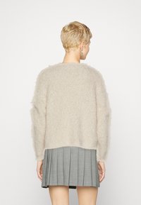 Beige, flauschiger Pullover mit lockerer Passform und strukturierten Oberfläche, mit überschnittenen Schultern und geradem Saum, kombiniert mit einem plissierten grauen Rock.