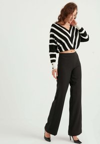 Randig svart och vit kortärmad tröja med V-ringning, tillsammans med högmidjade svarta byxor och spetsiga svarta klackar.