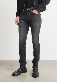 Jean ajustado negro de denim, con cinco bolsillos, cremallera en la bragueta y un leve desgaste. Combinados con mocasines negros.