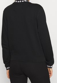 Sudadera negra con cuello redondo, puños acanalados y una banda estampada alrededor del cuello. Tejido suave y ajuste holgado.