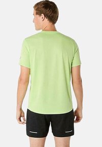 T-shirt verde chiaro a maniche corte con scollo tondo, abbinato a pantaloni corti neri con dettagli bianchi. Il tessuto appare liscio e leggero.