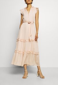 Vestido maxi rosa claro con mangas de volantes, cierre de botones, cintura con cinturón y volantes en capas en el dobladillo. Hecho de tela fluida.