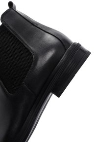 Botín Chelsea de cuero negro con un panel lateral elástico texturizado y un tacón bajo en forma de bloque. Acabado liso con detalles de costura sutiles.