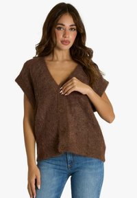 Cardigan marrone in maglia soffice con maniche corte e scollo a V profondo. Presenta bottoni in legno e una vestibilità ampia, abbinato a jeans blu.