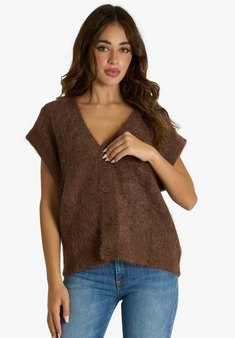 Cardigan marrone in maglia soffice con maniche corte e scollo a V profondo. Presenta bottoni in legno e una vestibilità ampia, abbinato a jeans blu.