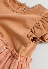 Robe couleur pêche à manches bouffantes courtes, avec un haut en coton lisse et une jupe froncée et texturée, dotée d'un ourlet à volants.