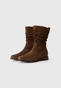 Stivaletti alla caviglia in suede marrone con design sformato, tacco piatto, punta arrotondata e dettagli di cucitura sottili. Ideali per un look casual.
