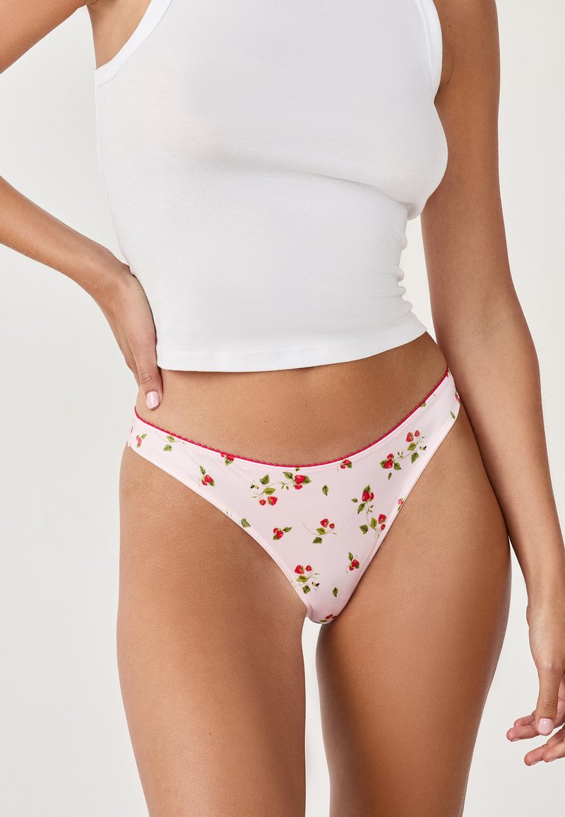 Rosa gemusterter Tanga mit kleiner roter Blumendruck, ergänzt durch rote Nähte am Bund, aus glattem, dehnbarem Stoff.