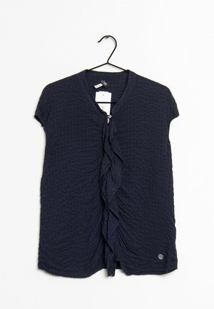 Haut à manches courtes bleu marine avec un design texturé et matelassé, comportant un détail en volant sur le devant et une fermeture à boutons décoratifs.