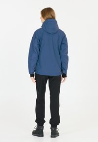 Sjöblå huva jacka med avslappnad passform, med elastiska muddar och en slät yta, tillsammans med svarta byxor och stövlar.