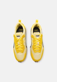 Puma Sneakers mit einem oberen Teil aus gelbem Textil, schwarzen Akzenten und weißer Sohle. Inklusive gelben Schnürsenkeln und einem Zungenlabel mit Logo.