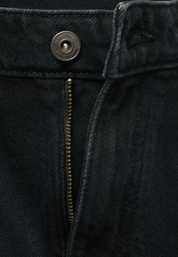 Prim-plan al unui material denim închis la culoare, cu un fermoar metalic și un nasture, evidențiind cusături detaliate și textură.