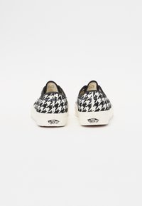 Mustvalge houndstooth mustriga slip-on tossud, kangast ülemine osa, kummist põhi, kontrastsete valgete aktsentidega ja brändi logo kontsadel.