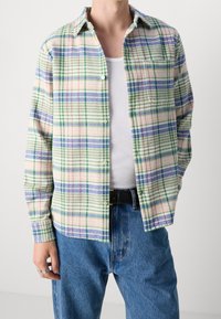 Koszula na guziki w kremowym kolorze w kratę, z niebieskimi, zielonymi i czerwonymi paskami. Wykonana z miękkiego materiału o luźnym kroju, z jedną kieszenią na piersi.
