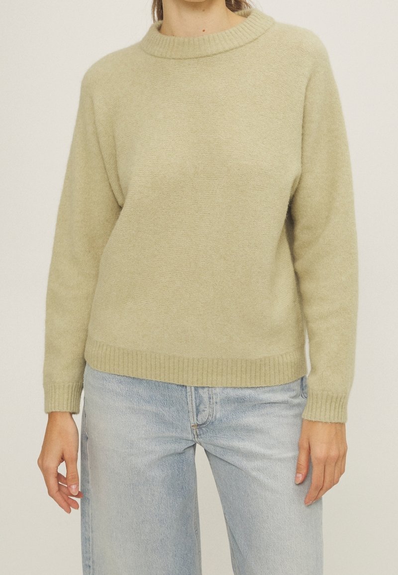 Ljusgrön stickad tröja med ribbat rundhals och muddar. Har en avslappnad passform och mjuk textur. Matchas med ljusblå jeans.
