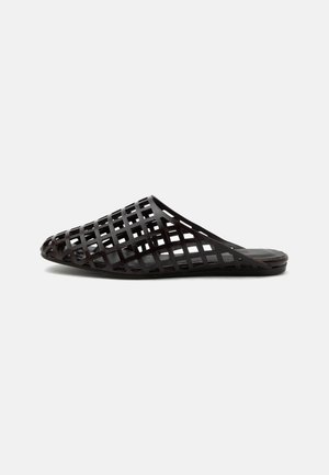 Zwarte slip-on sandaal met een puntige neus en een ruitvormig uitgesneden ontwerp, platte zool en open hiel op een effen achtergrond.