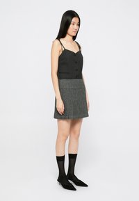 Svart knappetopp i camisole-stil, kombinert med et grått rutete skjørt med folder. Modellen har på seg svarte gjennomsiktige sokker og svarte spisse sko.