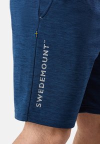 Marinblå shorts i texturerad tyg, med en silverfärgad logotyp tryckt på sidan och en liten svensk flagga som accent.