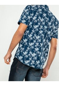 Camicia a maniche corte di colore blu navy, con un motivo di palme bianche. Realizzata in tessuto leggero, con colletto classico e vestibilità rilassata.