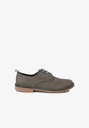 Scarpa in suede grigia con punta arrotondata, lacci grigi e suola in gomma marrone chiaro. Texture liscia, con accenti di cucitura minimal sui lati.