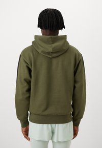 Sweatshirt verde-oliva com capuz ajustável e punhos texturizados. Apresenta detalhes em preto nas mangas e um acabamento texturizado.