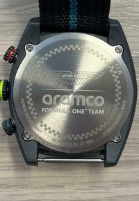 Stalowa tylna część zegarka z wygrawerowanym napisem "Aston Martin" oraz "aramco FORMULA ONE™ TEAM", z teksturowanym czarnym paskiem z kolorowymi akcentami.