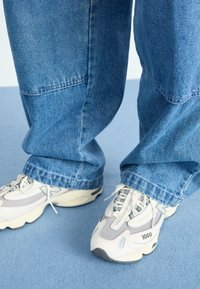 Baskets avant-gardistes en maille blanche et grise avec des semelles épaisses, associées à un jean en denim bleu à coupe décontractée et texture délavée.