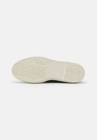 Semelle de chaussure noire avec un motif texturé comportant des formes surélevées et des rainures ; section beige clair au niveau du talon ; marque de taille 37 visible.