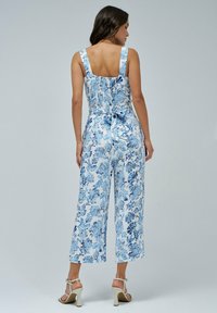 Jard ín de flores en azul y blanco, con piernas anchas, escote cuadrado y tirantes ajustables; cuenta con un respaldo fruncido y un detalle anudado.