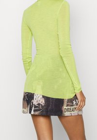 Langärmliges Kleid mit einem oberen Teil aus transparentem Neon-Grün und einem gemusterten unteren Abschnitt in Schwarz und Grau mit grafischen Details und Text.